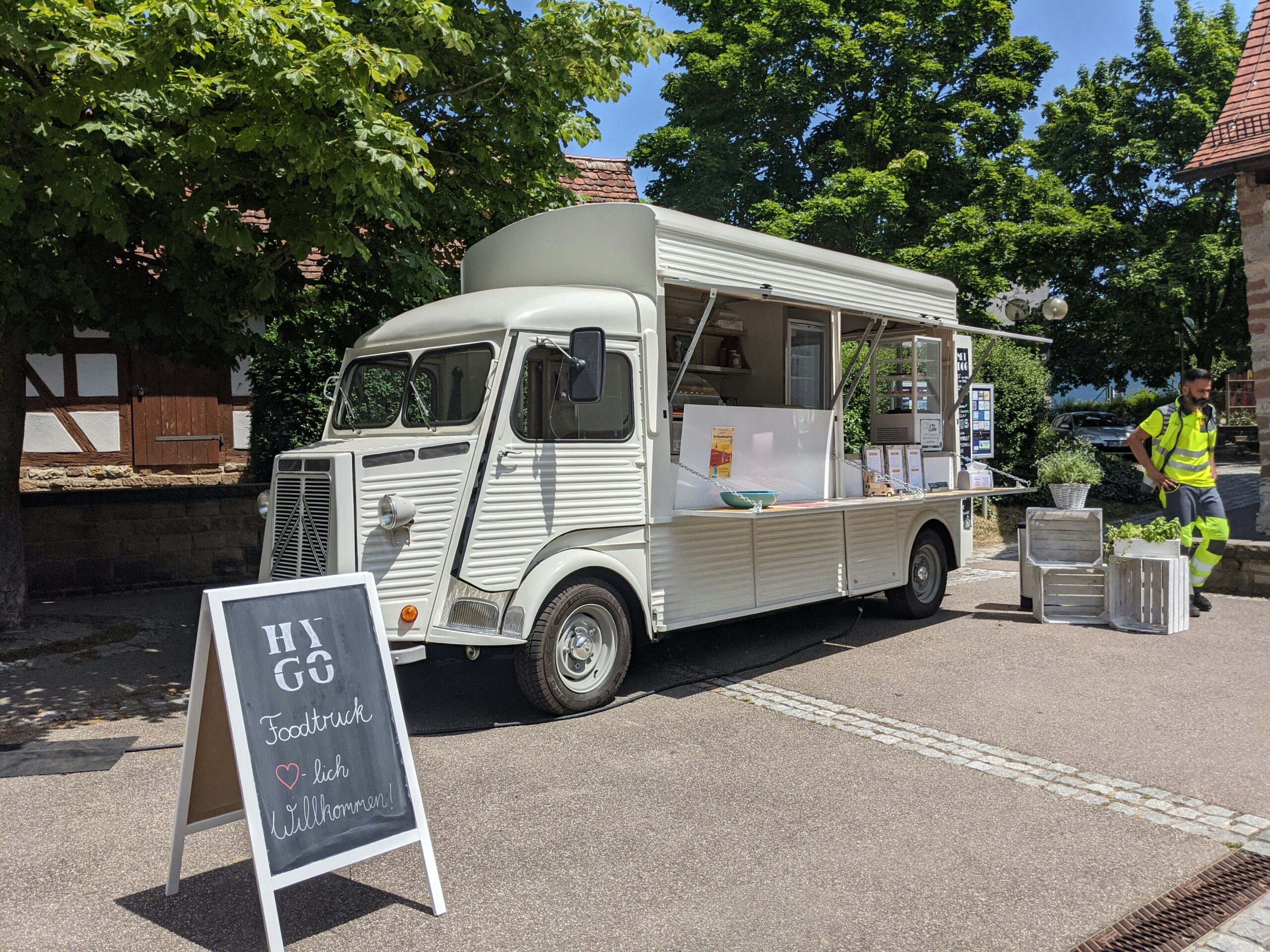 Hellgrauer Foodtruck unter einem Baum bittet Erfrischungen an