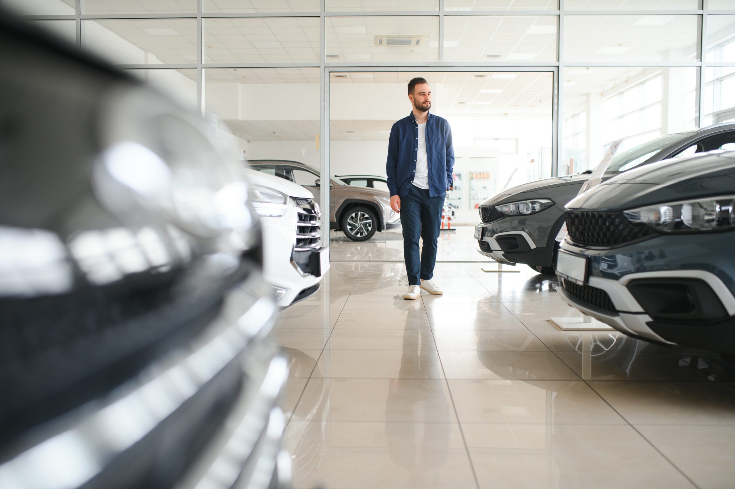 Ein junger Mann betrachtet ein Auto in einem Autohaus und prüft die Details, andere Fahrzeuge im Hintergrund.