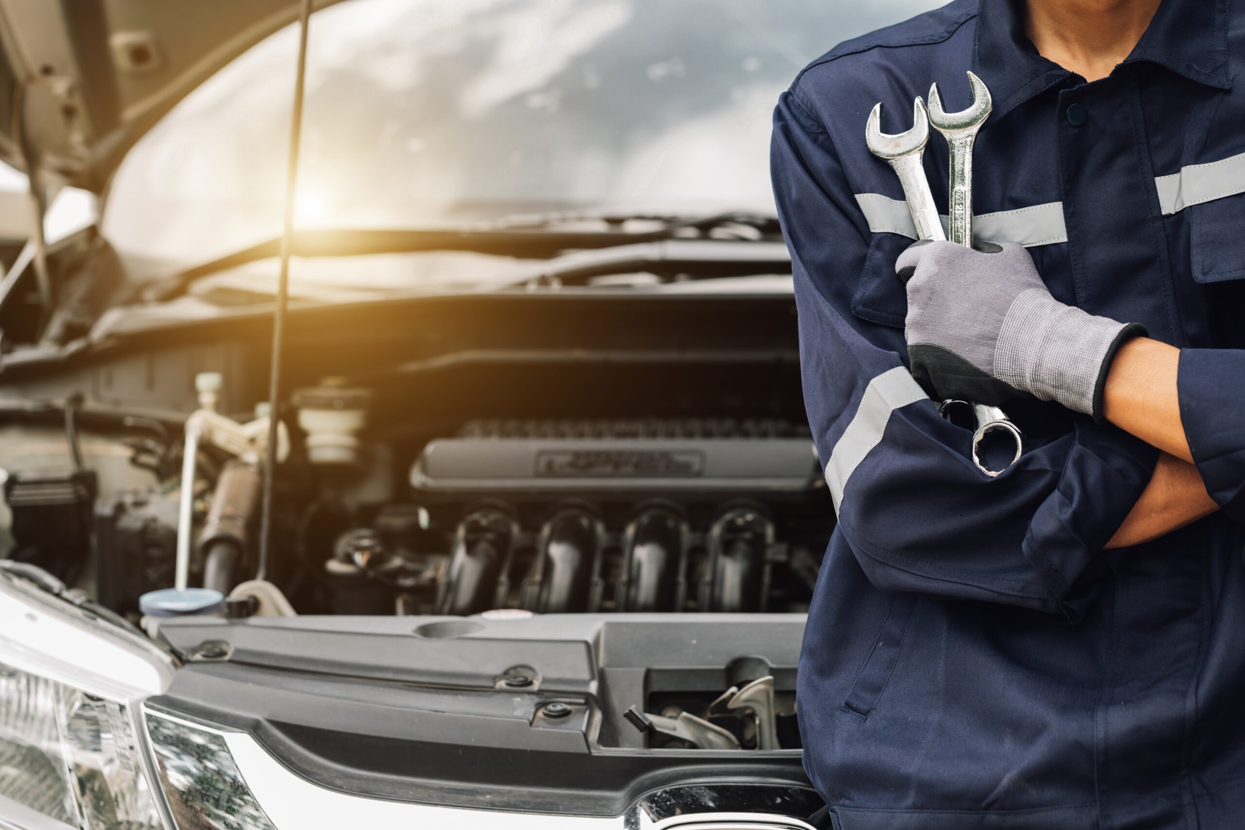 Hand eines Automechanikers mit Schraubenschlüssel bei der Arbeit in einer Autowerkstatt.