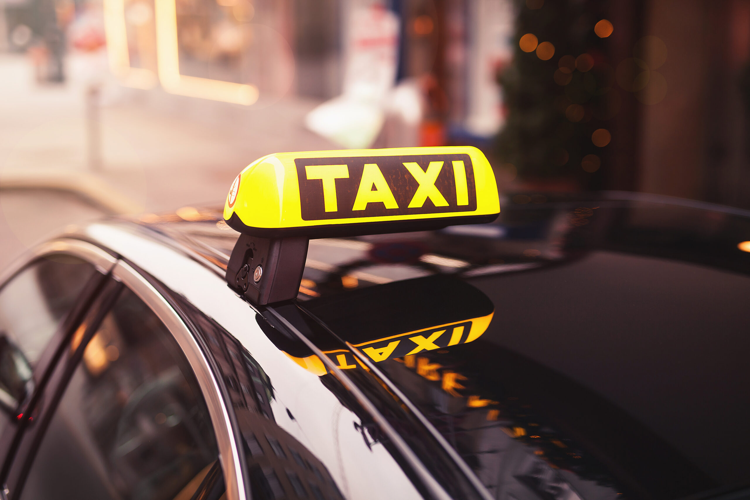 Gelbes Taxischild auf einem Autodach bei Nacht, mit verschwommenen Lichtern im Hintergrund.